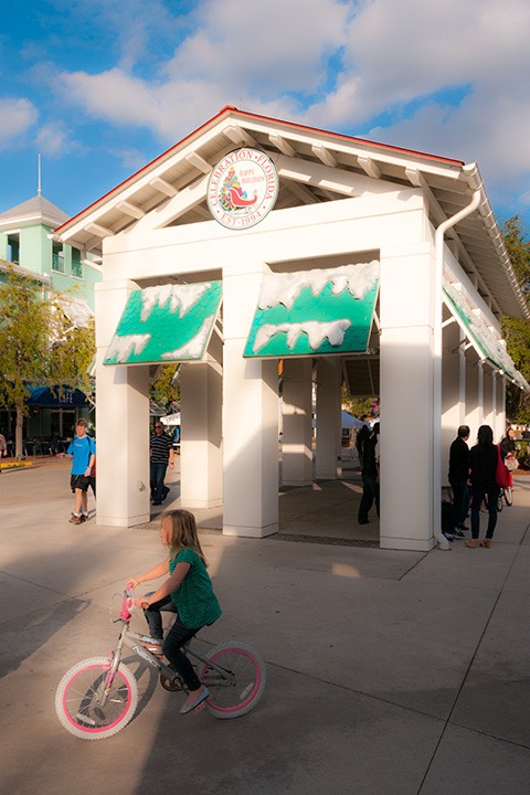 young girl on bicycle with pink-rimmed wheels cycles by Celebration, Florida market hall