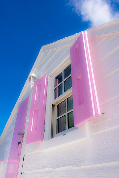 intense pink-shuttered door and window set against white gable stretch toward the sky above Dunmore Town on Harbour Island in the Bahamas