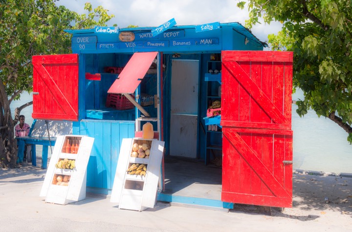 tiny single-crew grocery store with glistening red shutters opened against sea-blue shop structure on Bay Street, Dunmore Town on Harbour Island in the Bahamas