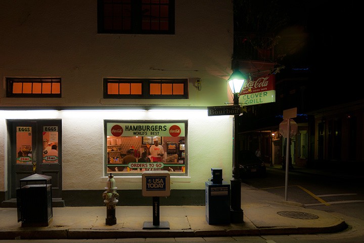 Clover Grill in New Orleans' French Quarter glows softly orange from within, while lit by blue-white light of corner street lamp against the gathering night