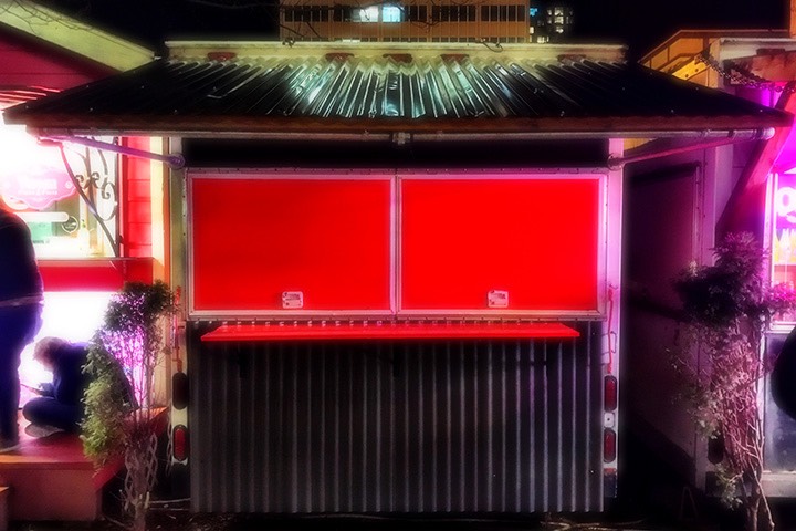 night lights glisten on the corrugated canopy roofing of Dinner Bell Barbecue food cart in Portland, Oregon, with window shutters glowing red just below