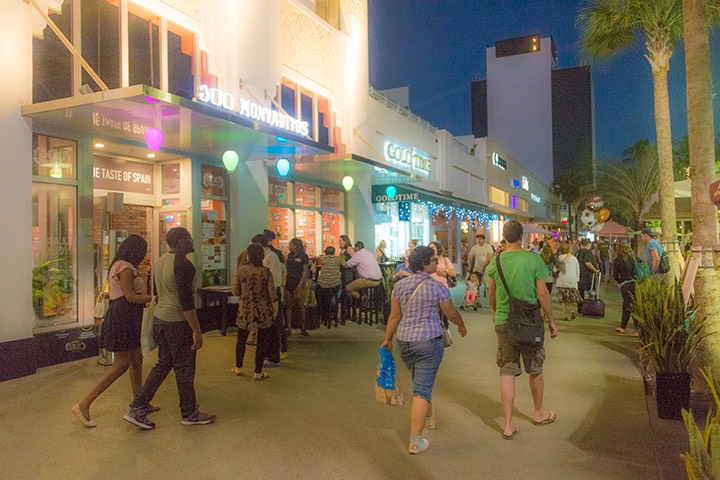 Miami Beach tourists walking along Lincoln Road as twilight descends beyond brightly-lit storefronts