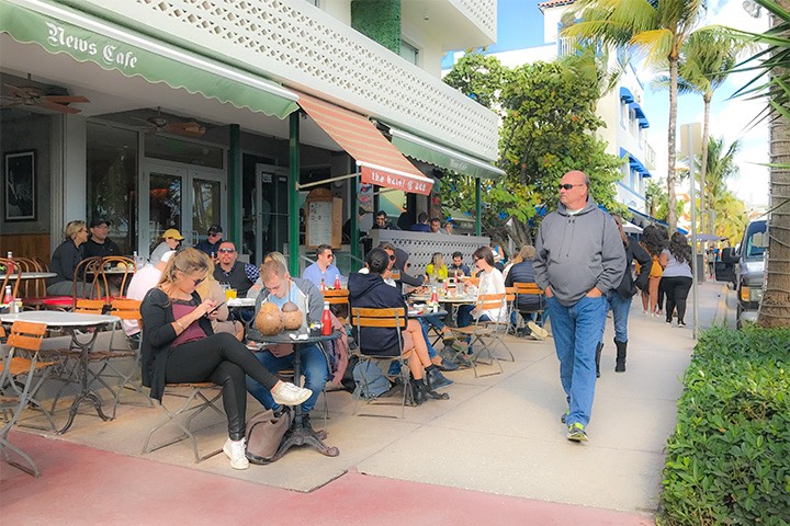 tourists stroll along Ocean Drive on South Beach as patrons enjoy brunch at the News Cafe